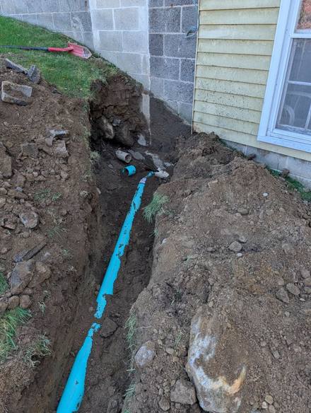 Trench along a block foundation with blue drain pipe