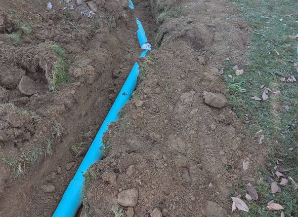 Blue drain pipe running through a trench across the yard