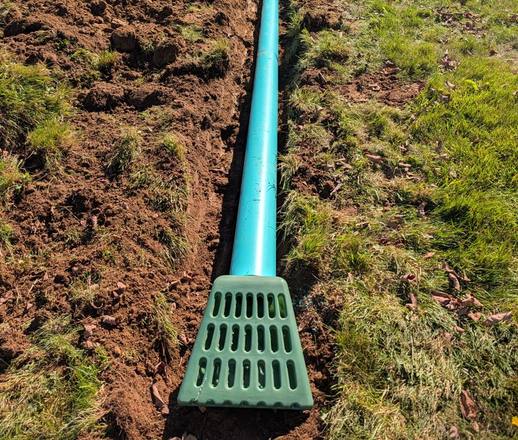 Drain pipe ending at a green grate outlet in the lawn