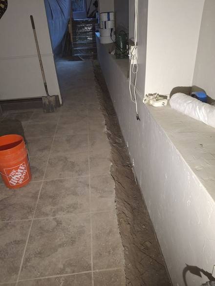 Trench cut through a tile floor along the wall of a finished basement