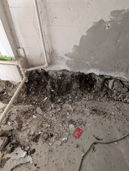 Basement wall with peeling paint and a trench being dug along its base
