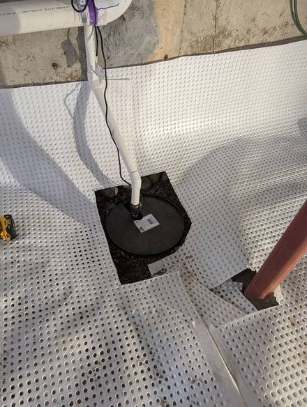 Dimpled drainage mat around a new sump basin with a discharge pipe