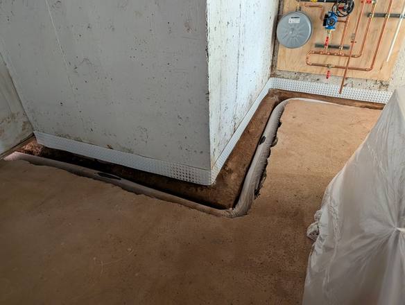 Drain pipe in a trench with a drainage strip at the base of the wall