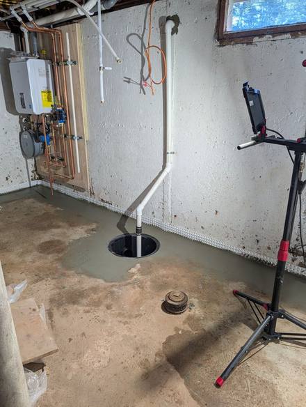 New sump basin with a discharge pipe and patched concrete floor